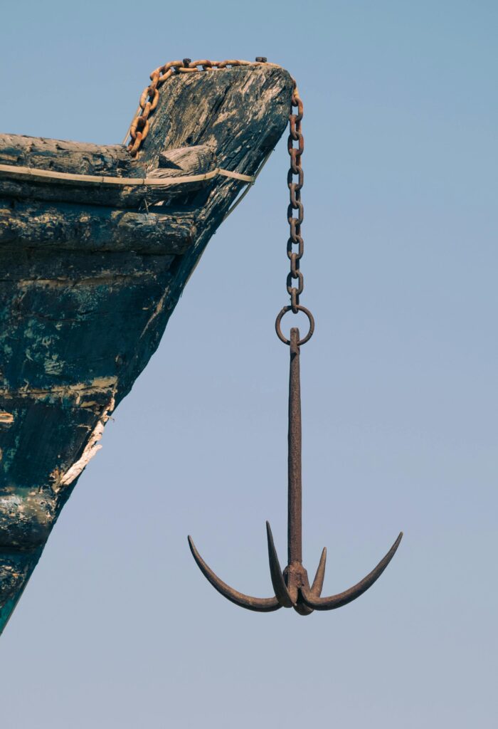Close-up of a boat's anchor dangling from an old ship under a clear sky.