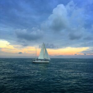 A serene sailboat glides on Key West's ocean at sunset, under a dramatic sky.